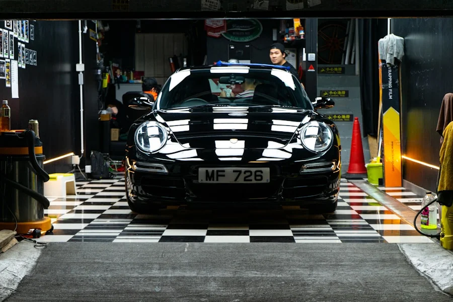 El mismo Porsche negro limpio, con pintura brillante y cristales claros, en el mismo taller y encuadre.