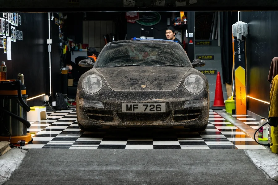 Porsche negro con polvo, residuos y marcas de agua en el frente y el parabrisas; imagen editada para demostración.